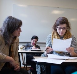 A student looking at a paper while professor looks on to guide.