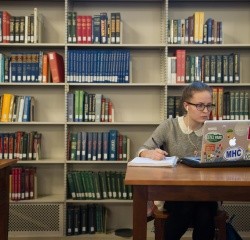 A student working in the library with a notebook and a laptop