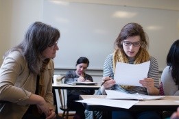 A student looking at a paper while professor looks on to guide.