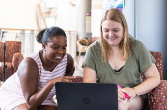 Two Professional Graduates students smiling, looking at a laptop screen