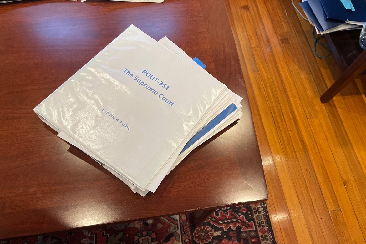 A white binder with a title page that reads "POLIT-351 The Supreme Court Danielle R. Holley" on a wooden table.