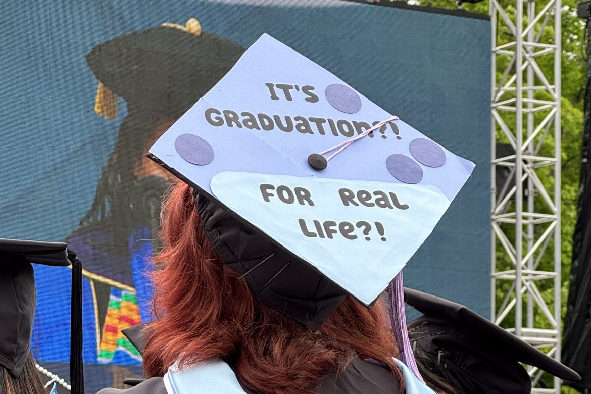 A 2024 graduate of Mount Holyoke College wearing a mortarboard decorated with the phrase “It’s graduation?! For real life?!”