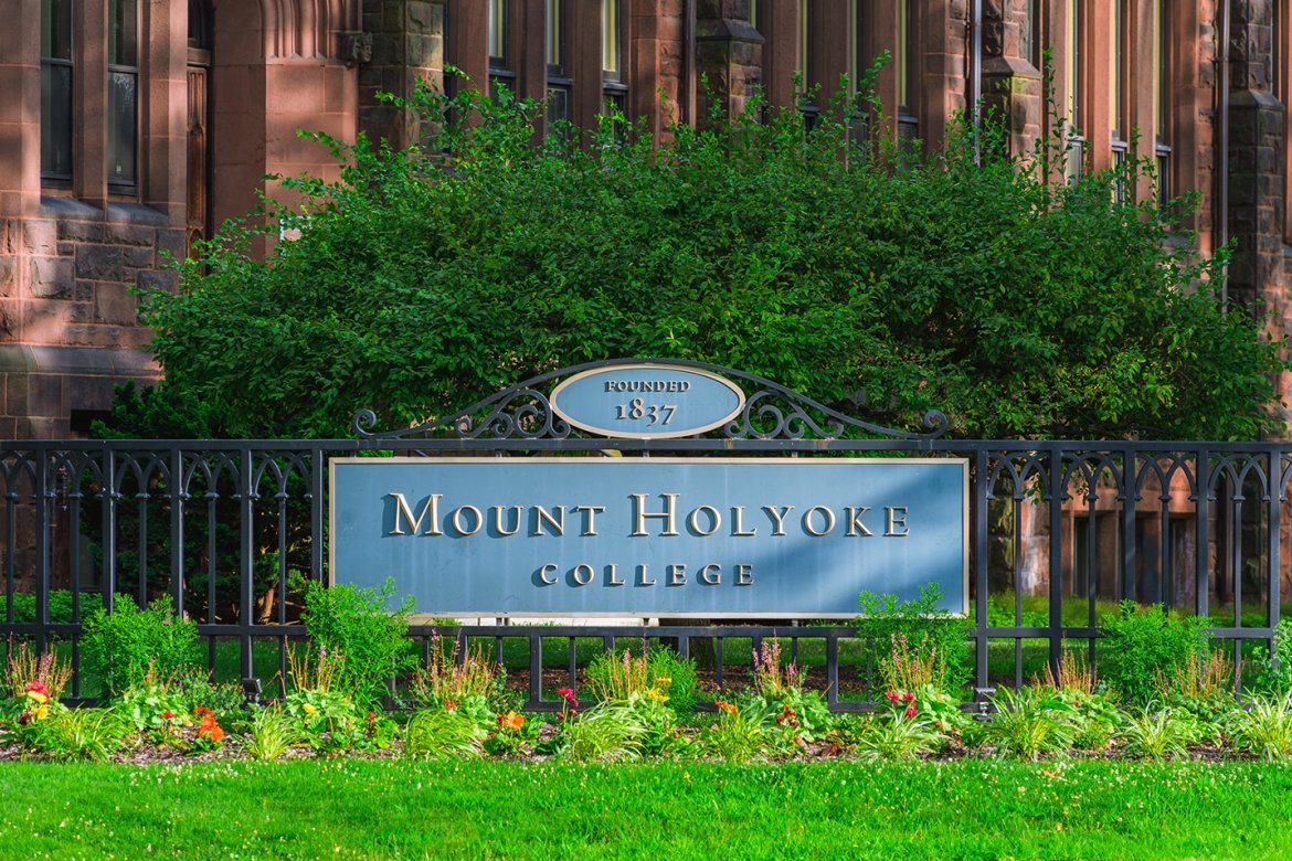 Mount Holyoke College sign in the summer of 2024 with a vibrant green tree behind it.