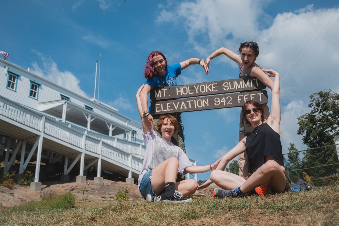 Students making a heart shape with their arms around the Mt. Holyoke state park sign. Mountain Day 2024. Photo by Max Wilhelm.