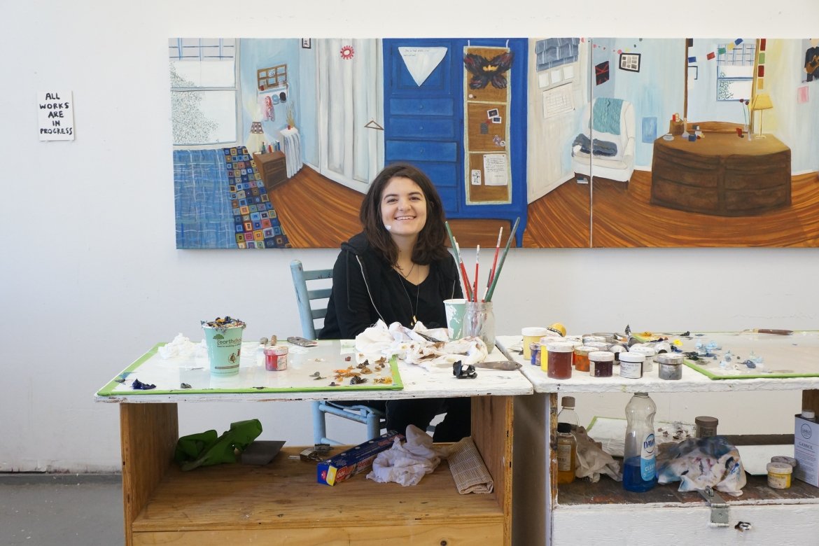 Anna Berlin ’15 sitting at a desk surrounded by art. 