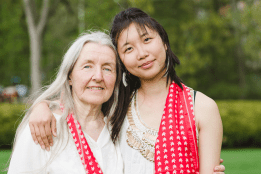 An alum and a student embracing with matching red scarves