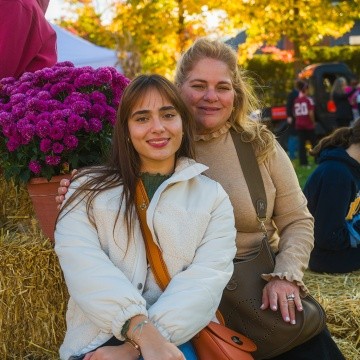 Student and family member sit on decorated hay bales at Mount Holyoke's Fall Fest in 2024.