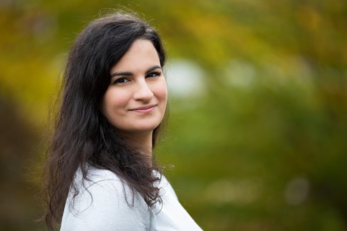 Katerina Drakoulaki, a woman with long dark brown hair, wearing a white shirt and smiling at the camera.