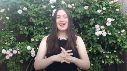 Graduating senior Casey Roepke addresses her fellow celebrants. She stands outside, smiling in front of a blooming rose bush.