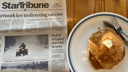 A plate of pancakes and newspaper sitting on a table