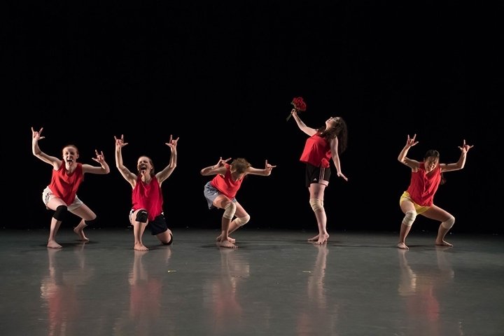 Five dancers, crouching onstage, with arms overhead bent at right angles.