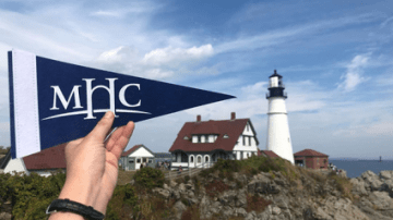 MHC flag in front of a seaside building with a lighthouse.